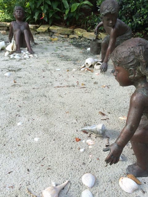 Three small bronze statues of children at the beach