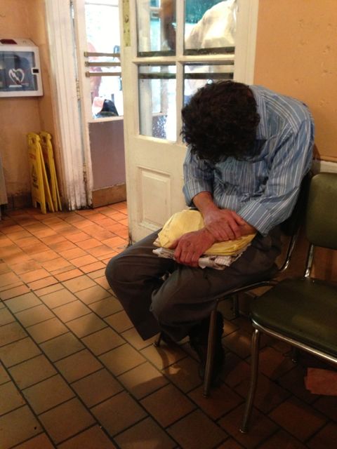 exhausted, overworked, from trying to simply get by day to day homeless man sitting asleep inside Cafe Du Monde
