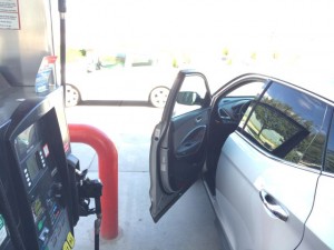 Rental car at gas station with door open at pump