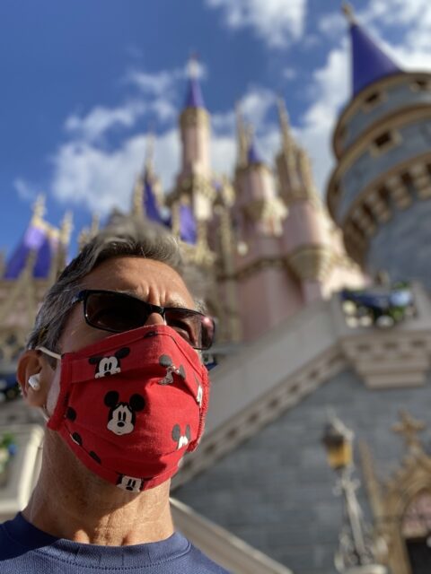 Man in a Mickey Mouse face mask next to Cinderella Castle